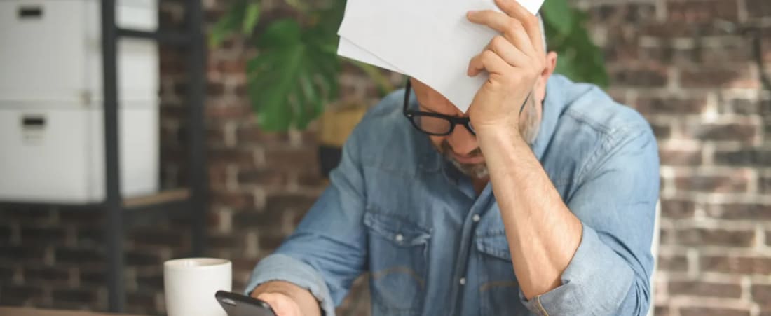 Man in a denim shirt holding a stack of papers to his bowed head