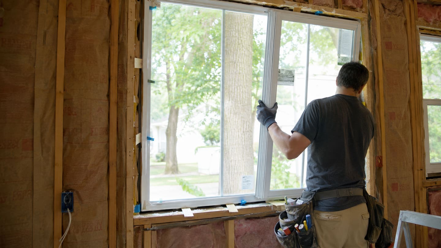 Man in gloves guiding a white sliding window into a framed opening